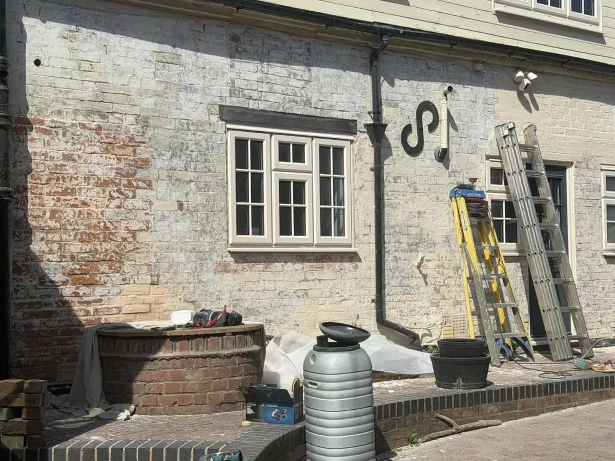 Modern masonry paint being stripped back to bare brick, ladders against the wall