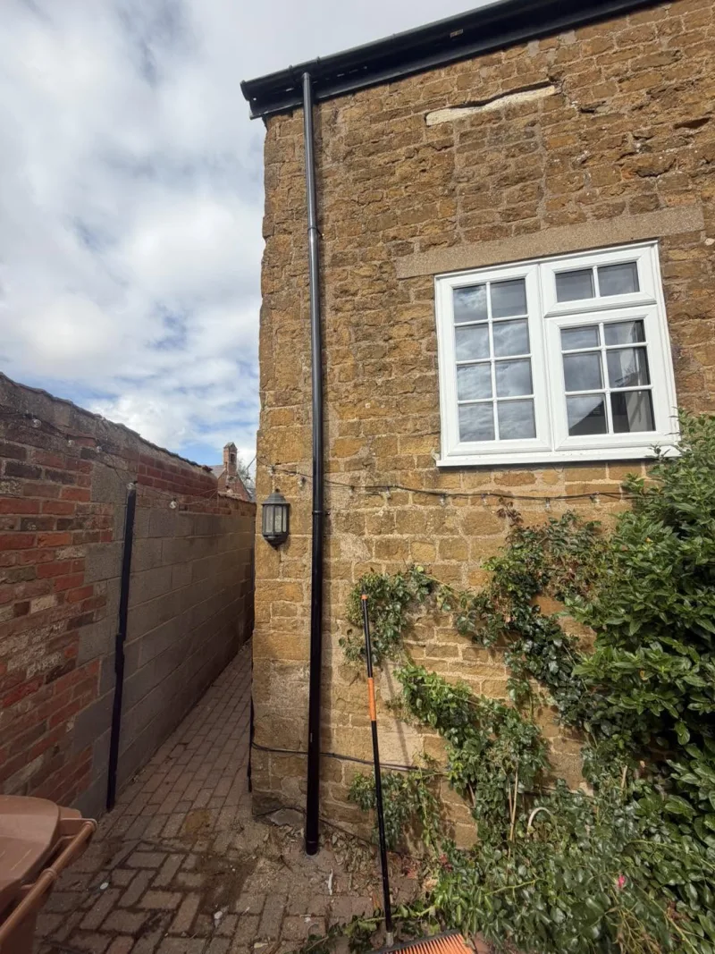 Golden ironstone cottage wall repointed in lime, with a black cast iron downpipe